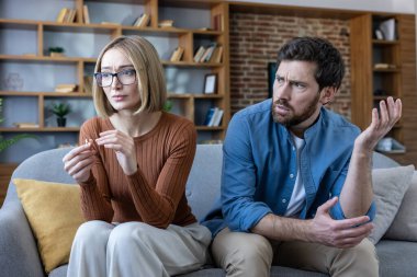 Evde ilişki sorunları yaşayan bir çift, üzgün bir kadın boşanma yüzüğü tutarken üzgün bir adam tartışırken, ayrılığı ve evlilik sorunlarını sembolize ederken
