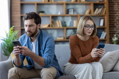Çift kanepeye oturuyor, ekranlara bakıyor, her biri akıllı telefonlarına gömülüyken duygusal olarak uzak ev ortamında dijital kopukluk, kayma, mesajlaşma ve izolasyon