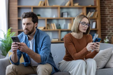 Çift, akıllı telefonlarına dalmış, ilişkilerde iletişim bozukluğu ve teknoloji bağımlılığını gösterirken, evde oturup birbirini görmezden geliyor.