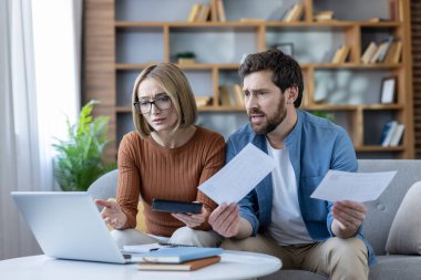 Evde faturaları ve mali belgeleri inceleyen, dizüstü bilgisayar ve hesap makinesindeki harcamaları hesaplayan, kredi kartı borçlarıyla boğuşan ve ekonomik kriz sırasında potansiyel iflasla boğuşan çift.