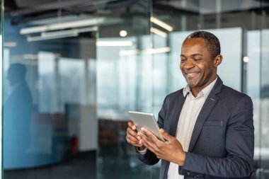 Deneyimli iş adamı, portatif bir tabletle iletişim kurarken gülümsüyor, kurumsal çalışma ortamında modern teknoloji ve bağlantı sergiliyor.