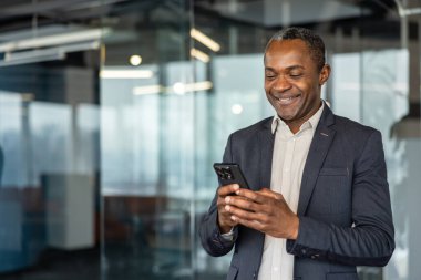 Modern bir ofis binasında yönetici olarak çalışan, cep telefonunu profesyonel iletişim ve ağ kurmak için kullanan, çağdaş iş yerinde başarı ve teknolojiyi temsil eden bir adam.