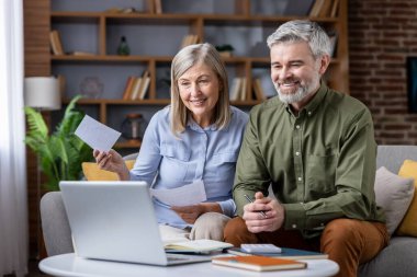 Üst düzey çift oturma odalarındaki koltukta oturuyor, gülümsüyor ve dizüstü bilgisayarla çalışıyor, ev finansmanlarını yönetiyor, faturaları gözden geçiriyor ve aylık bütçe planlarını tartışıyorlar.