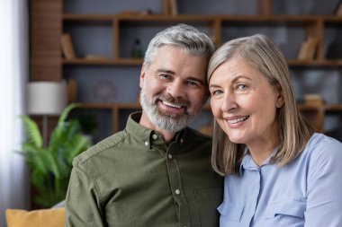 Gülümseyen olgun çift evlerinde sıcak bir kucaklaşmayı paylaşıyor. Sevgiyi, memnuniyeti ve refakati paylaşıyorlar. Rahat günlük hayatlarında ve emekliliklerinde.