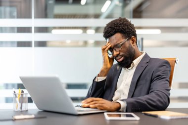 Genç adam, bir dizüstü bilgisayarla çalışırken işyerinde hayal kırıklığı ve zihinsel yorgunluk yaşıyor. Kurumsal bir ortamda stres, patinaj ve baskı tasvir ediyor.
