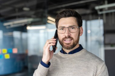 Gözlüklü ve süveterli bir adam çağdaş bir ofis ortamında modern iletişimi, iş ağını ve uzaktan çalışmayı temsil ediyor.