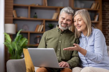 Üst düzey bir çift kanepede dinleniyor. İnterneti, video görüşmelerini, alışveriş merkezlerini gezmek ve aile ve modern teknoloji ile bağlantılarını koparmamak için dizüstü bilgisayar kullanırken gülümsüyorlar.