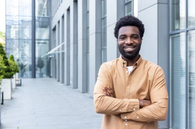 Kolları çapraz duran girişimci, modern bir mimari arka plana karşı güvenle gülümseyen, kentsel bir çevrede başarı, iş ve profesyonel hedefleri temsil eden