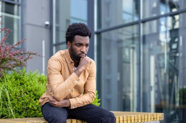 Dışarıda oturan genç adam, zor kararlar verirken ya da stresli bir durum yaşarken, endişe ve endişe hissederek yaşamdaki zorlukları yansıtıyor.