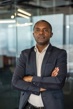 Deneyimli profesyonel bir adam kollarını kavuşturmuş, modern ofis ortamında güven ve otorite aktarıyor, iş dünyasındaki liderlik ve başarıyı simgeliyor.