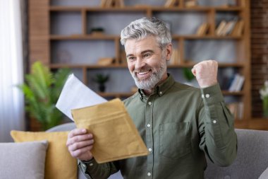 Evdeki kanepede oturan mutlu kıdemli adam, bir zarf açıyor ve iyi haberlerle bir mektup okuyor, başarıyı veya başarıyı yumruğuyla kutluyor.