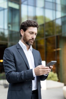 Akıllı telefon içeriğini gören bir iş adamı dışarıda dururken, teknolojiyle bağlantı kurarken, profesyonel görevleri yönetirken, ve şehir merkezinde modern iletişim kurarken,