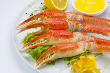 Haşlama yengeç pençeleri sos ve beyaz arka plan üzerinde bir tabakta limon ile