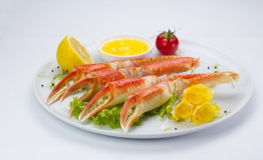Haşlama yengeç pençeleri sos ve beyaz arka plan üzerinde bir tabakta limon ile