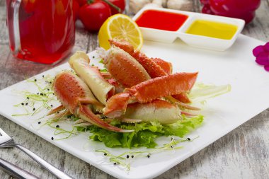 Haşlama yengeç pençeleri ahşap arka plan üzerinde lezzetli içki ile sos, limon ve kiraz domates ile