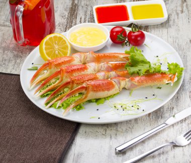 Haşlama yengeç pençeleri ahşap arka plan üzerinde lezzetli içki ile sos, limon ve kiraz domates ile