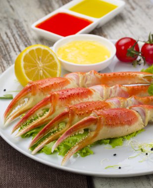 Haşlama yengeç pençeleri ahşap arka plan üzerinde lezzetli içki ile sos, limon ve kiraz domates ile