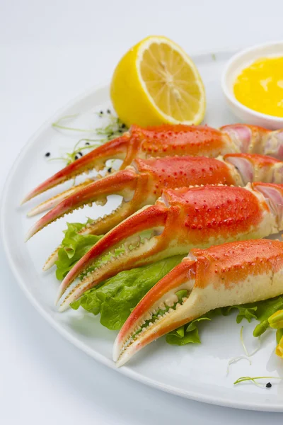 Garras de cangrejo hervidas con salsa y limón en un plato sobre fondo blanco — Foto de Stock