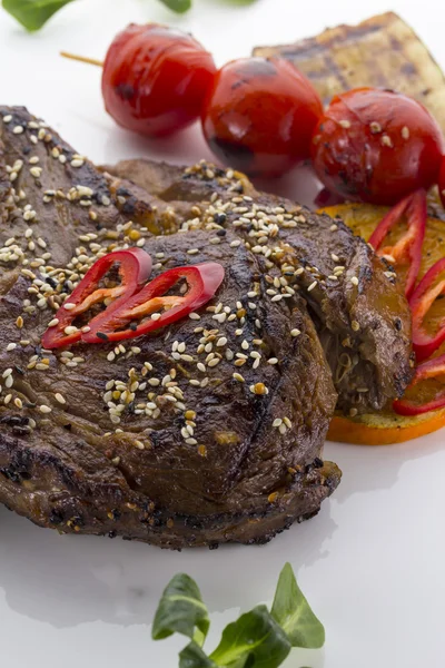 Biefstuk, geserveerd met tomaten en sesam op een witte plaat — Stockfoto