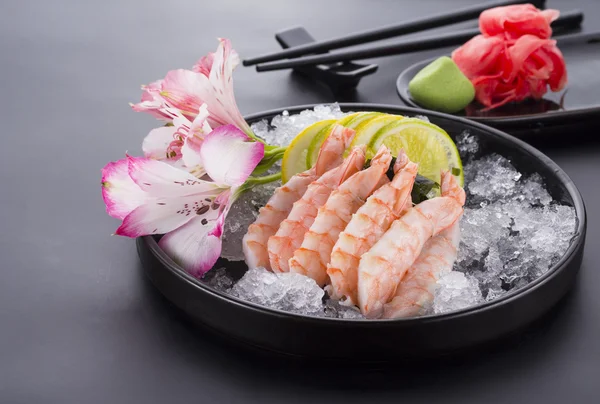Japanese cuisine, shrimp Sashimi with ice with ginger and wasabi on a black plate — Stock Photo, Image