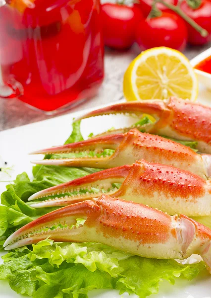 Haşlama yengeç pençeleri ahşap arka plan üzerinde lezzetli içki ile sos, limon ve kiraz domates ile