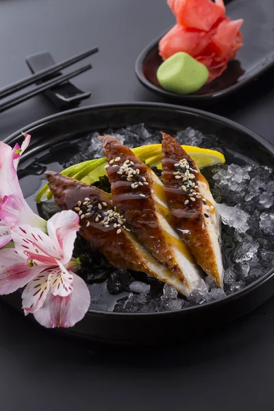 Sashimi de anguila con hielo sobre un plato negro con wasabi de jengibre sobre fondo negro —  Fotos de Stock