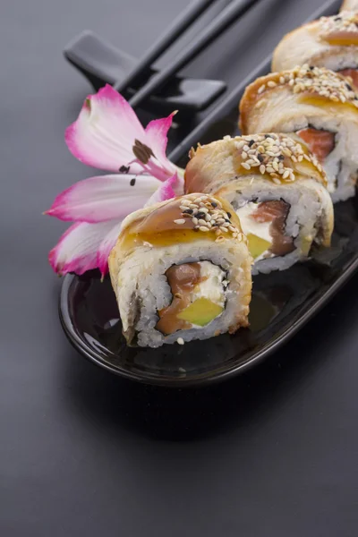 Rouleau de sushi d'anguille sur une plaque noire avec décoration florale — Photo