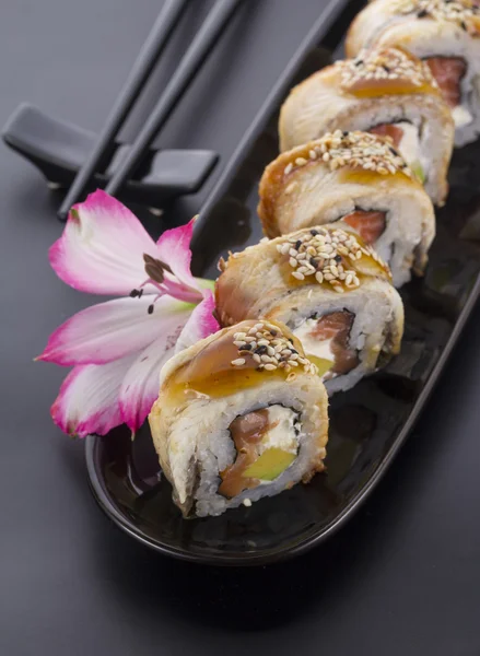 Eel sushi roll on a black plate with flower decoration — Stock Photo, Image