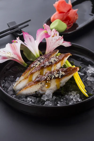 Aal-Sashimi mit Eis auf schwarzem Teller mit Ingwer-Wasabi auf schwarzem Hintergrund — Stockfoto