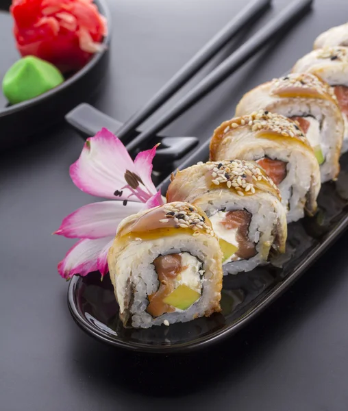 Rollo de sushi de anguila en un plato negro con decoración de flores —  Fotos de Stock