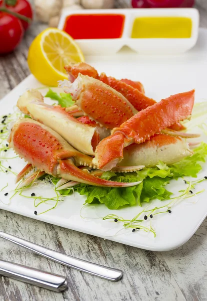 Garras de cangrejo hervidas con salsa, limón y tomate cherry sobre fondo de madera — Foto de Stock