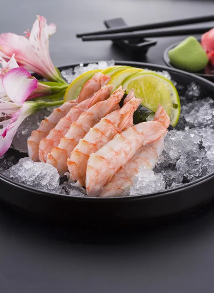 Japanese cuisine, shrimp Sashimi with ice with ginger and wasabi on a black plate — Stock Photo, Image