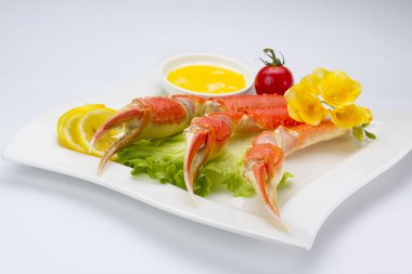 Haşlama yengeç pençeleri sos ve beyaz arka plan üzerinde bir tabakta limon ile