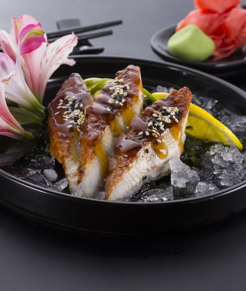 Sashimi de anguila con hielo sobre un plato negro con wasabi de jengibre sobre fondo negro —  Fotos de Stock