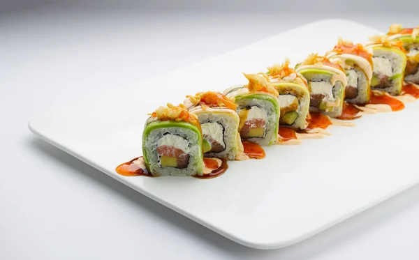 Sushi com salmão de abacate e queijo. Crunch Roll. Com deliciosos molhos. Em uma chapa sobre fundo branco . — Fotografia de Stock