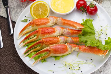 Haşlama yengeç pençeleri ahşap arka plan üzerinde lezzetli içki ile sos, limon ve kiraz domates ile