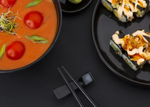 Japanese cuisine. Vegetarian soup with tomato and coconut and crunch sushi roll over black background