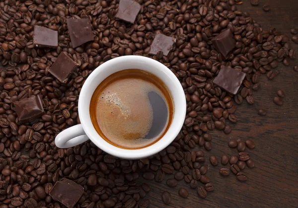 Uma chávena. Grãos de café e chocolate em uma mesa de madeira — Fotografia de Stock