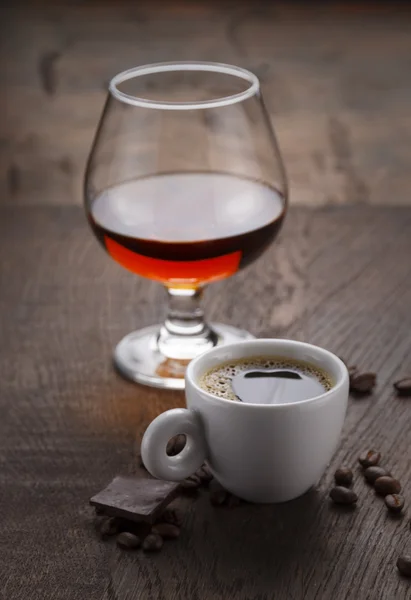 Φλιτζάνι καφέ, ποτήρι κονιάκ ή μπράντυ και κόκκους καφέ σε ένα ξύλινο τραπέζι — Φωτογραφία Αρχείου