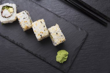 Suşi roll bir taş plaka üzerinde siyah arka plan üzerinde