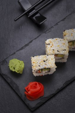 Suşi roll bir taş plaka üzerinde siyah arka plan üzerinde