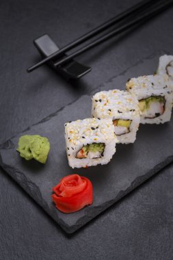 Suşi roll bir taş plaka üzerinde siyah arka plan üzerinde