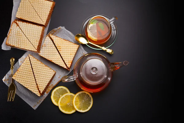 De driehoekige gebak zoet wafel met gecondenseerde melk en verse hete zwarte thee op een zwarte lijst — Stockfoto