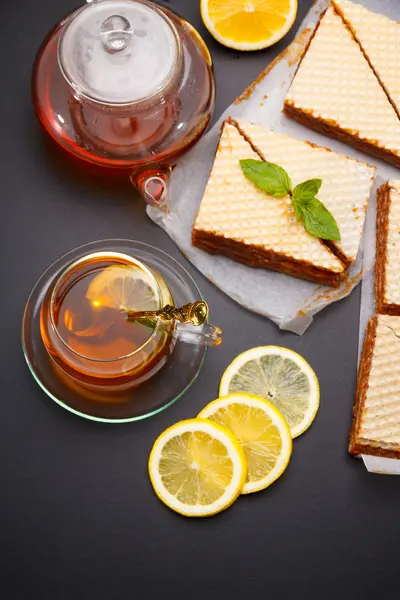Söt våffla trekantiga kakor med kondenserad mjölk och färsk het svart te på ett svart bord — Stockfoto