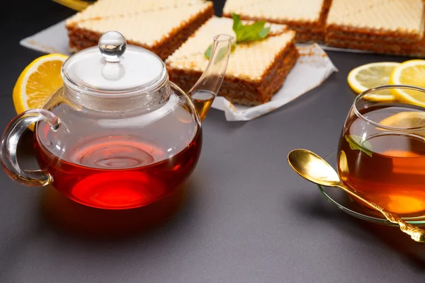 De driehoekige gebak zoet wafel met gecondenseerde melk en verse hete zwarte thee op een zwarte lijst — Stockfoto