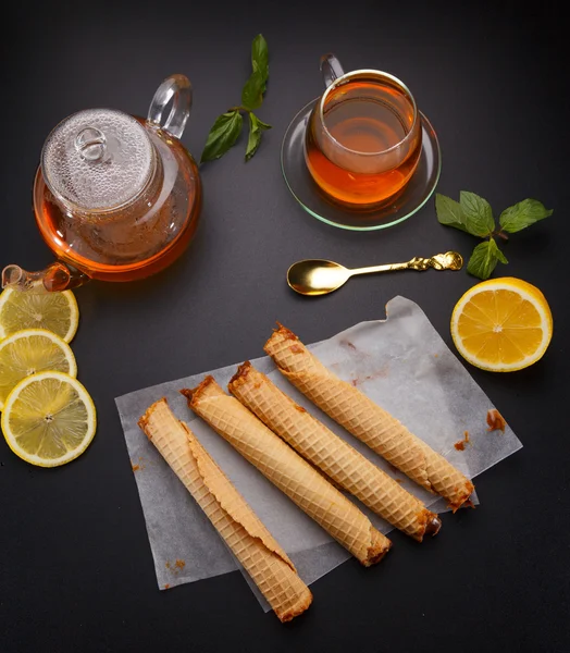 Túbulos de gofres con leche condensada y té caliente fresco y limón sobre fondo negro — Foto de Stock