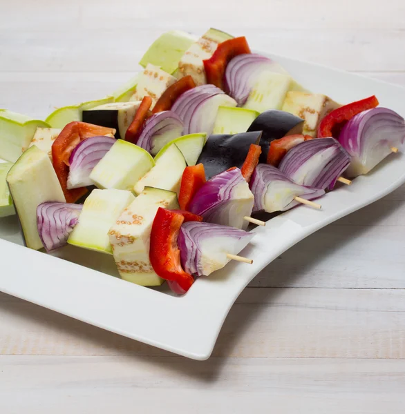 Szpikulec surowych warzyw na talerzu przez drewniane tła — Zdjęcie stockowe