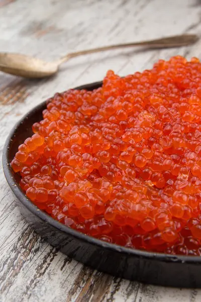 Röd kaviar i en svart plåt över en vintage bakgrund — Stockfoto