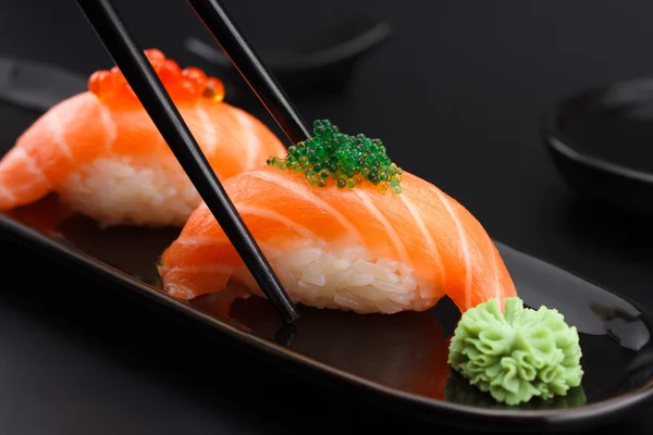 Salmon sushi nigiri in chopsticks over black background — Stock Photo, Image