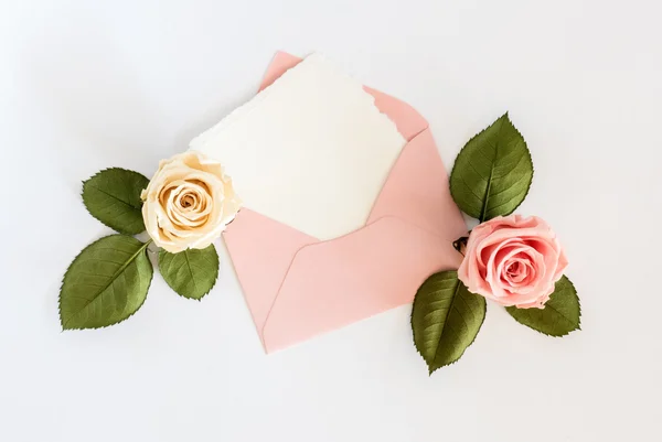 Roze envelop met witte kaart en rozen. Plat leggen. — Stockfoto